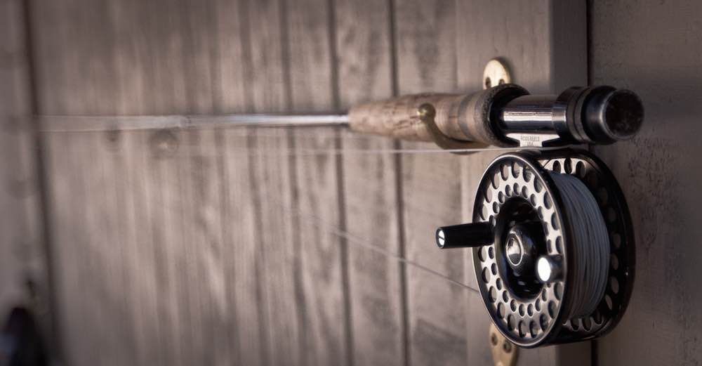 A fishing rod and reel are hanging on a wooden wall.