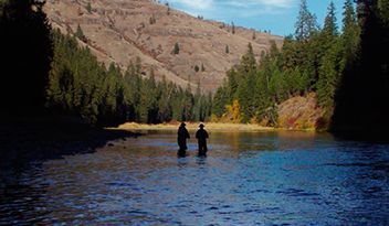 Two Men Are Fishing in A River with Mountains in The Background