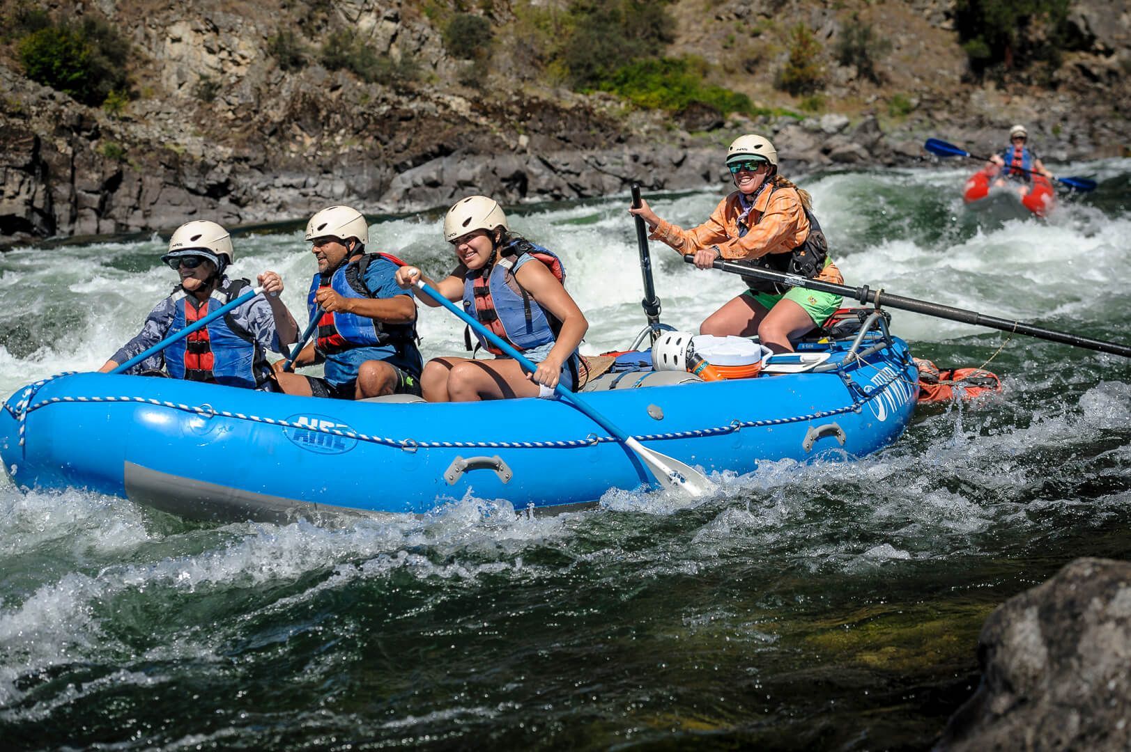 Four People Rafting Down a River in A Blue Raft