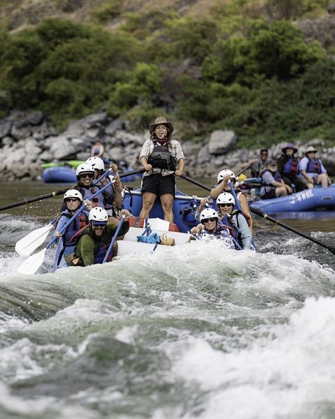 Group of People Rafting Down a River in Rafts with One Woman Standing