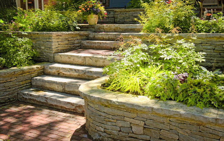 A stone wall surrounds a set of stairs in a garden.