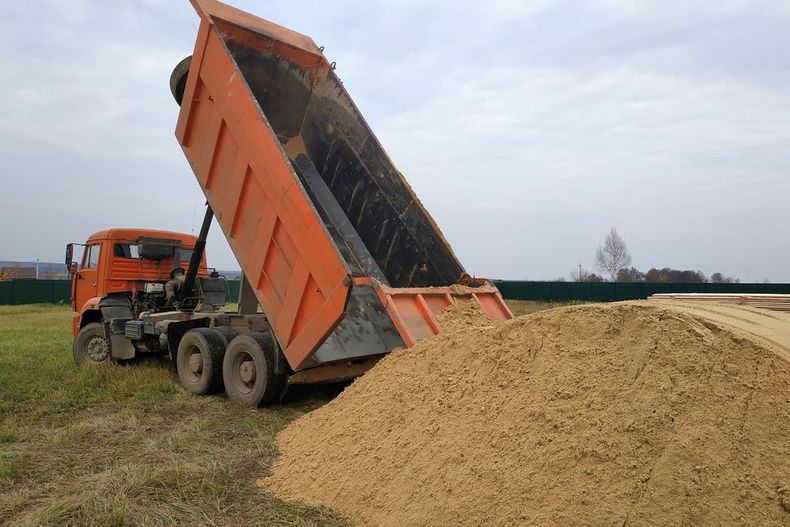 A dump truck is dumping sand in a field.