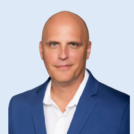 Man in a blue blazer and white shirt, smiling slightly, against a light blue background.