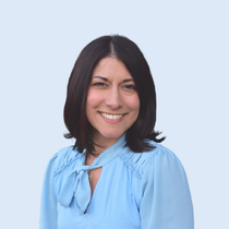 Woman with dark hair and a light blue blouse smiles, set against a light blue background.