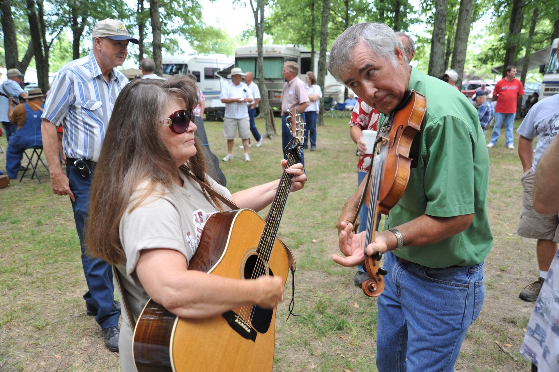 A woman is playing an acoustic guitar while a man plays a violin
