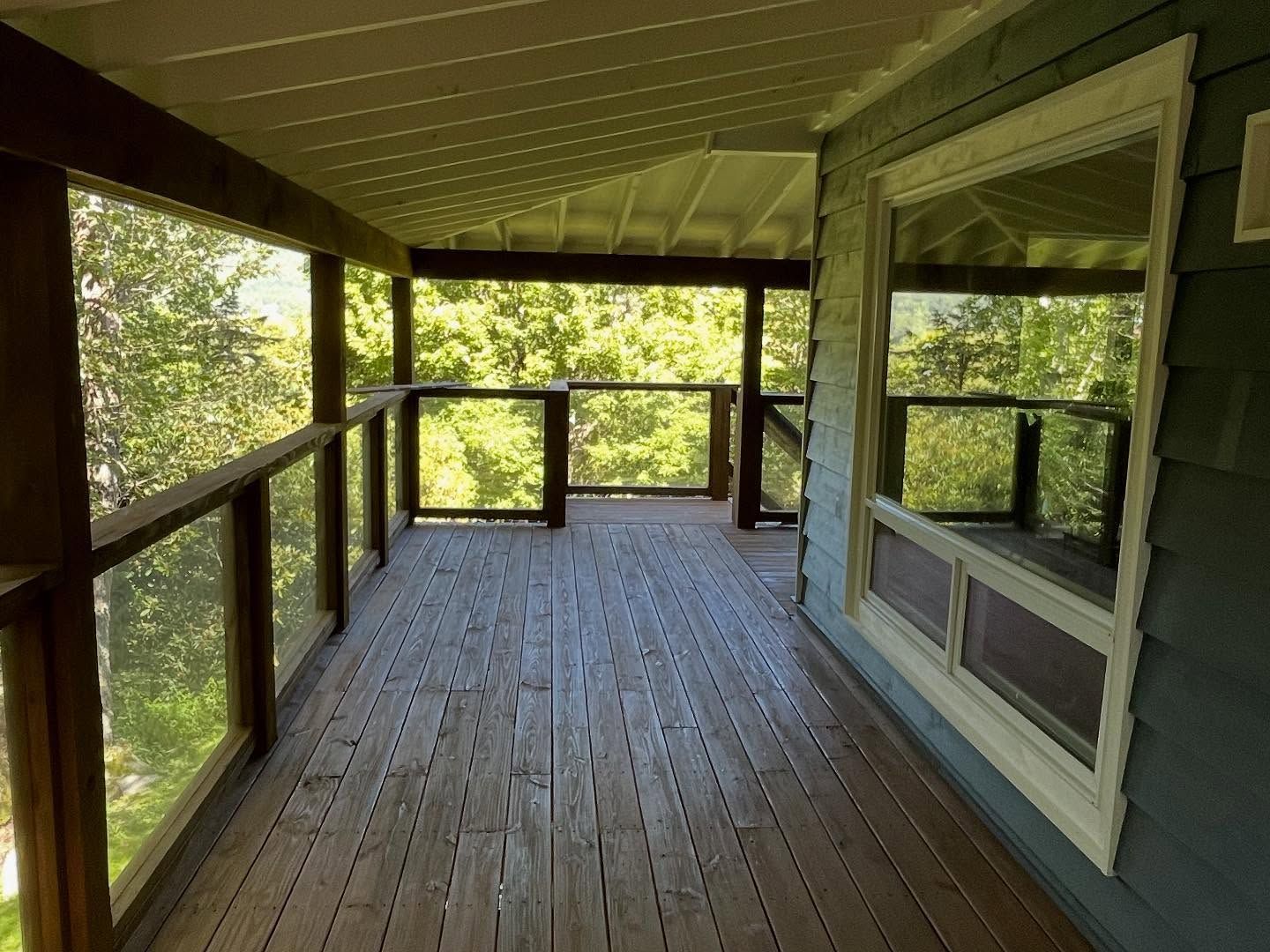 Wooden porch with glass railings and a large window overlooking trees.