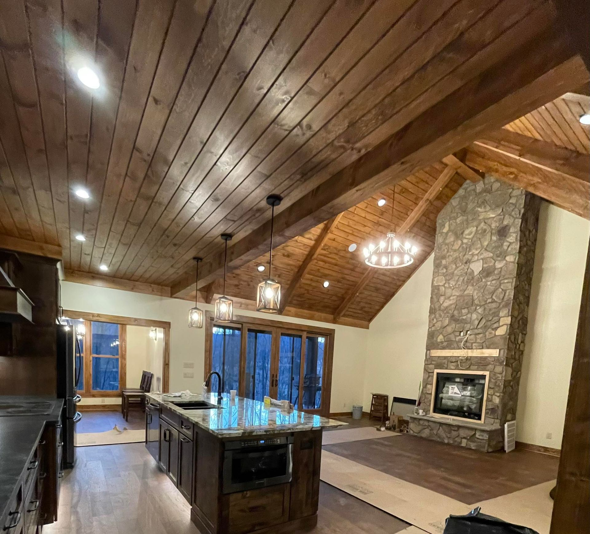 A rustic living space with a kitchen island, stone fireplace, and wood-beamed ceiling.