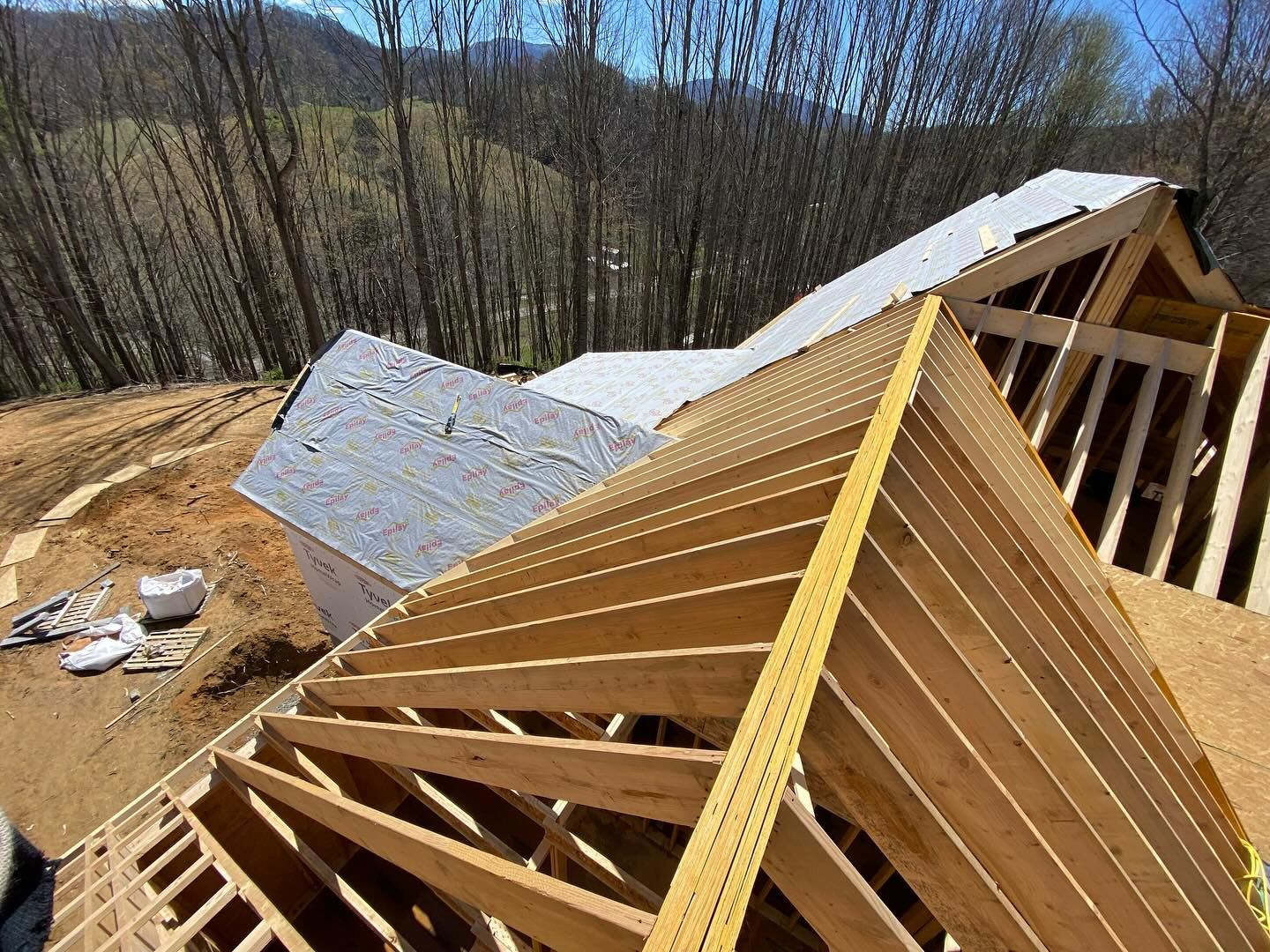 Wooden roof trusses under construction on a house, with a backdrop of trees and a bright sky.