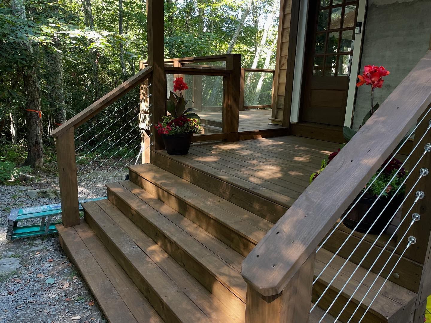 Wooden deck with stairs leading to a doorway. Red flowers in pots. Cable railing.