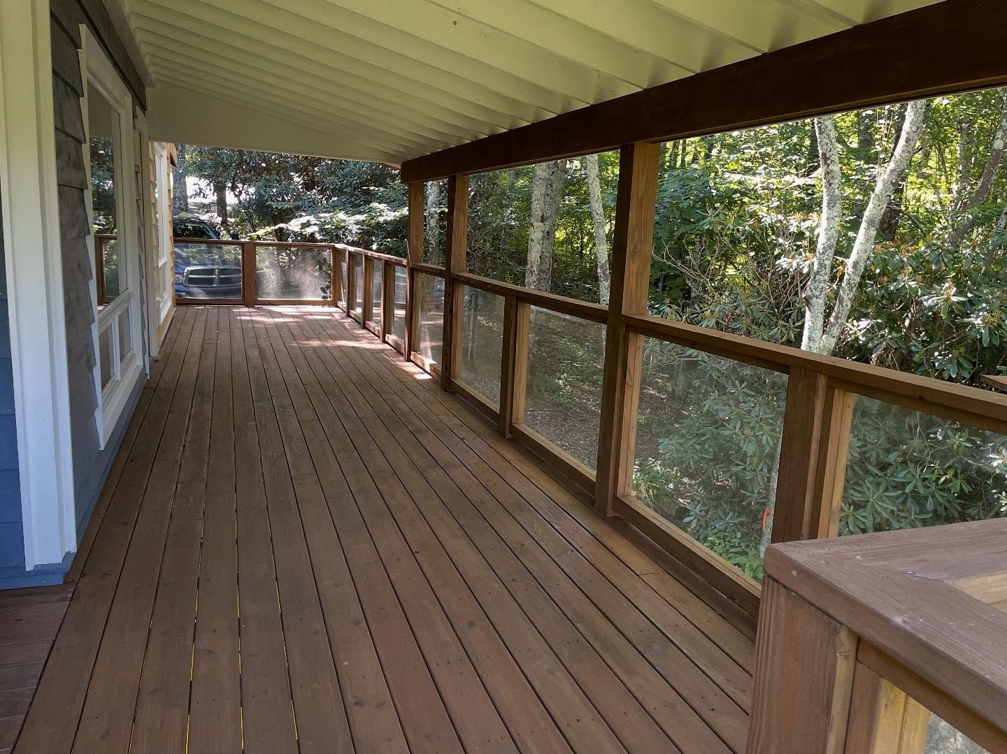 Wooden deck with glass railing, overlooking a lush green forest.