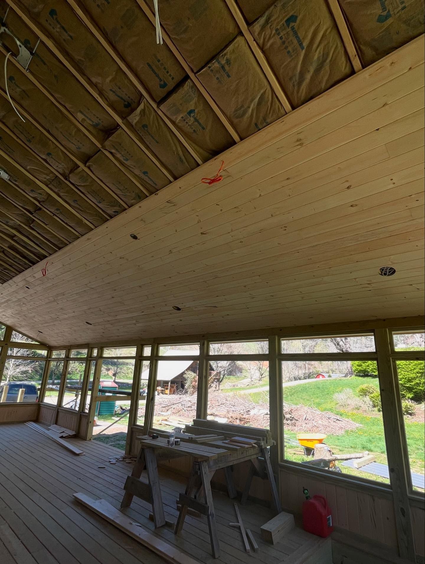 Sunroom under construction with wood plank ceiling and windows looking onto a yard.