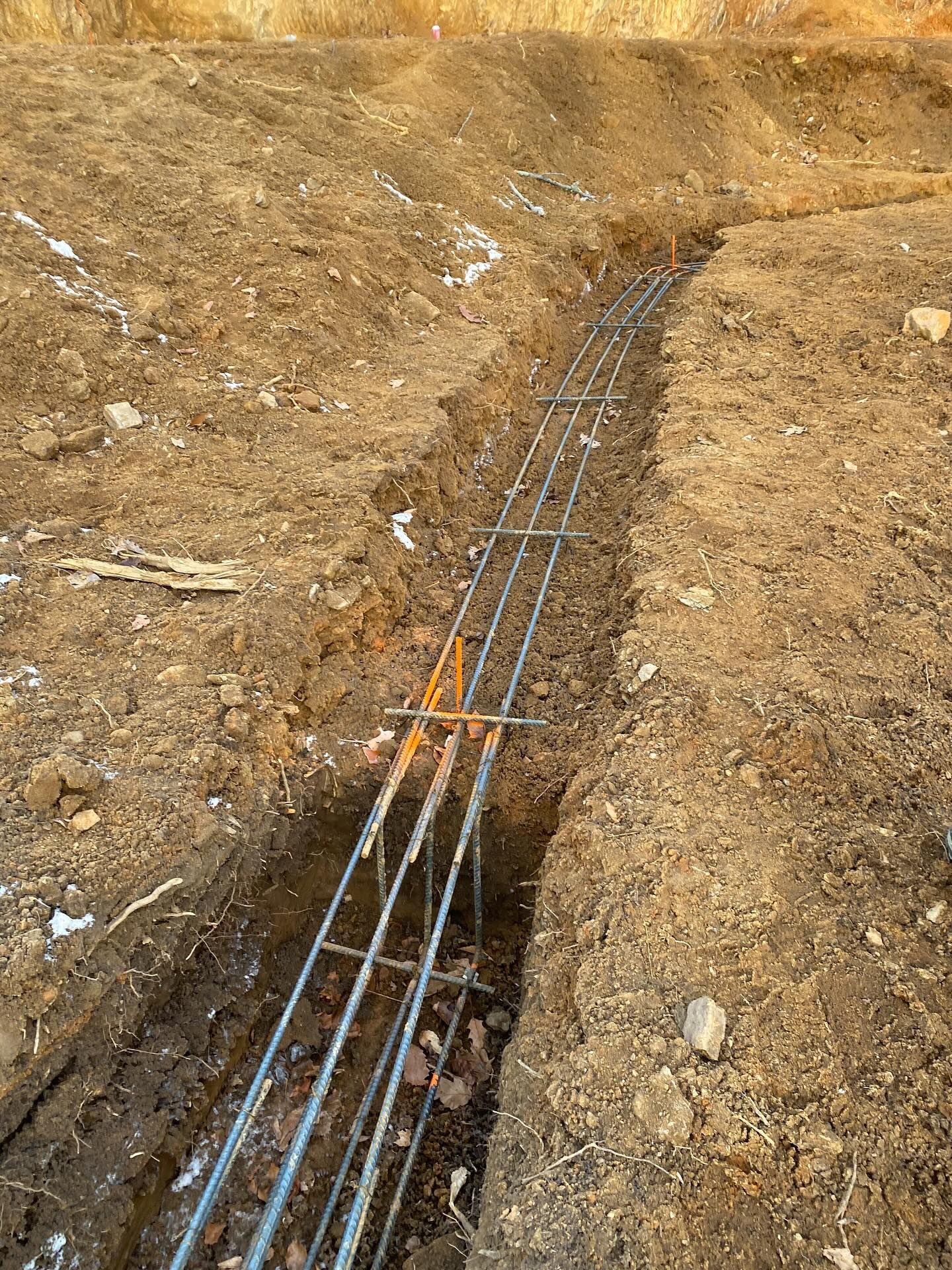 A trench dug in dirt, steel rebar framework installed for concrete foundation.