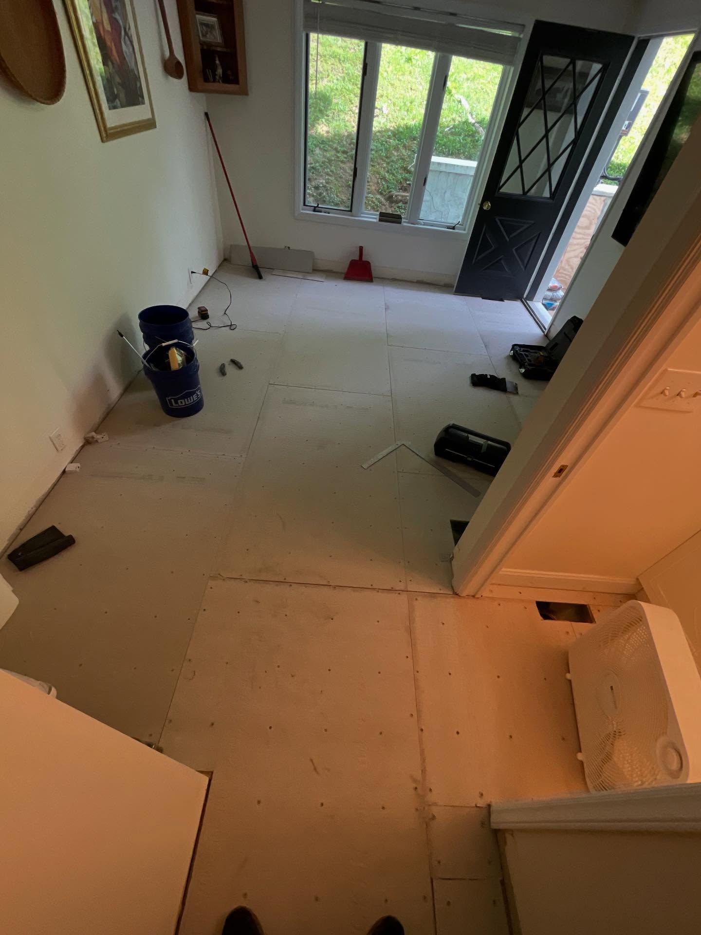 Interior view of a room with flooring removed, doorway, window, and supplies.