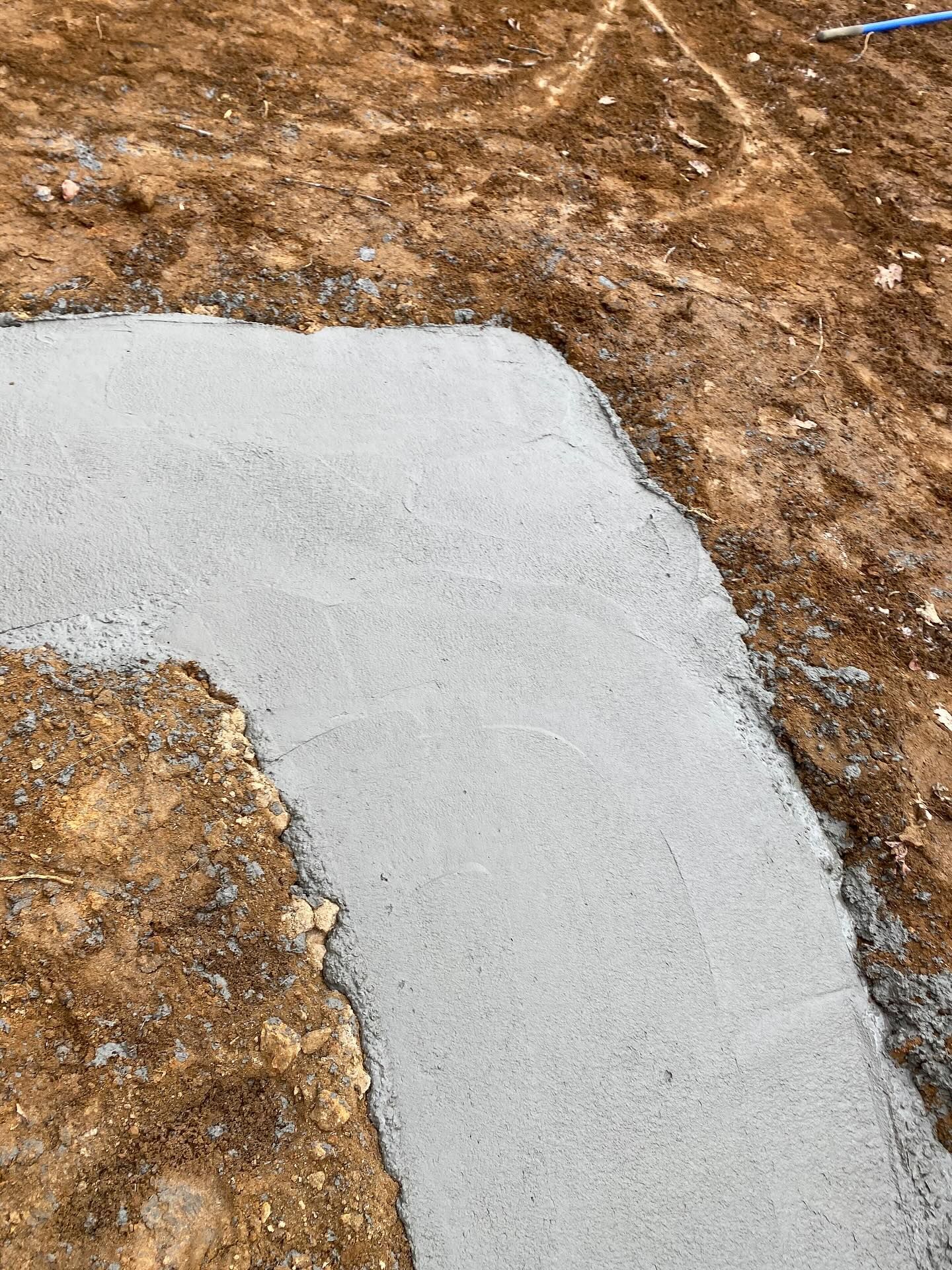 Newly poured concrete path, curving around a brown dirt area.