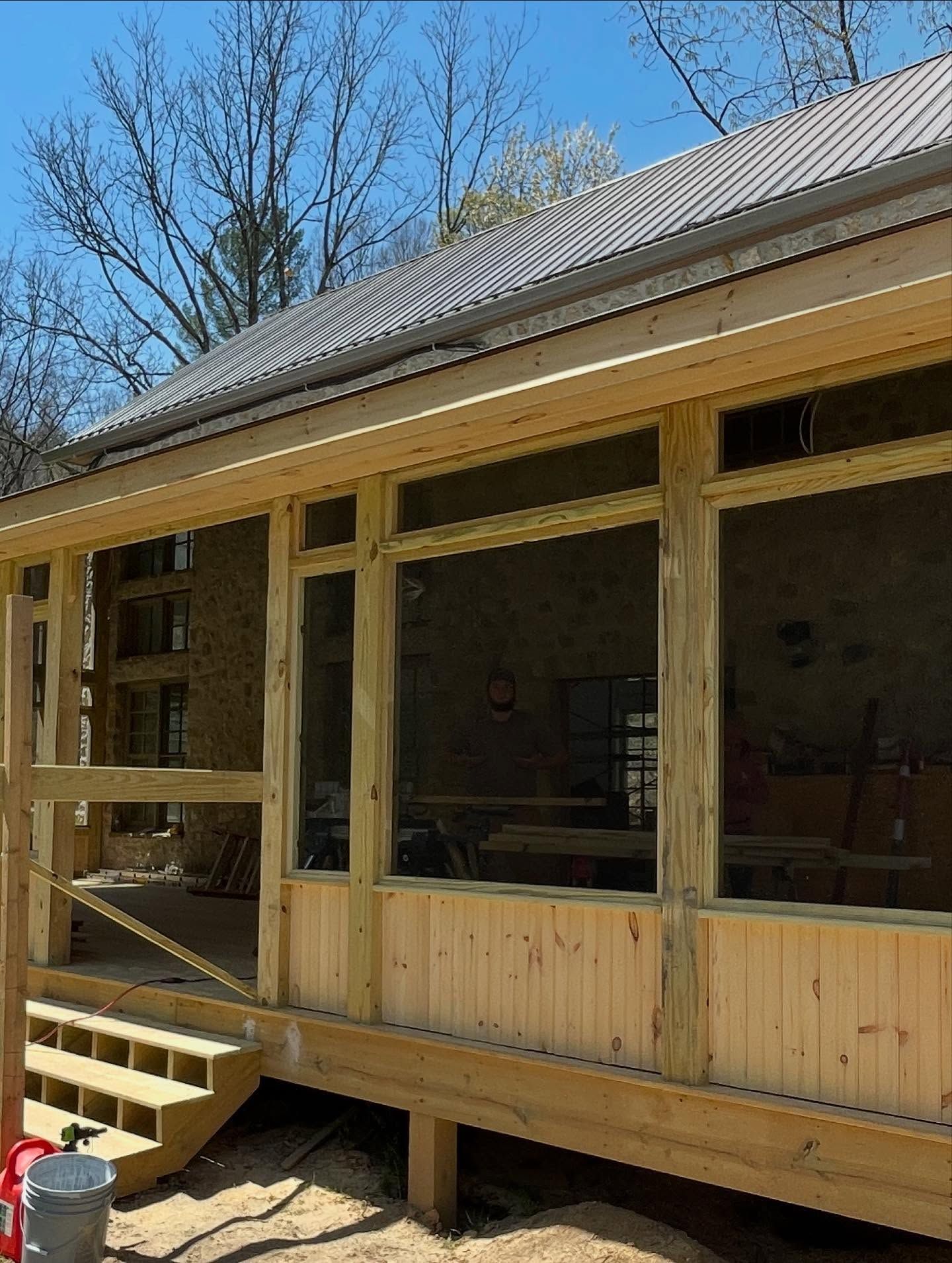 A wooden screened-in porch under construction, with steps leading down to a dirt ground.