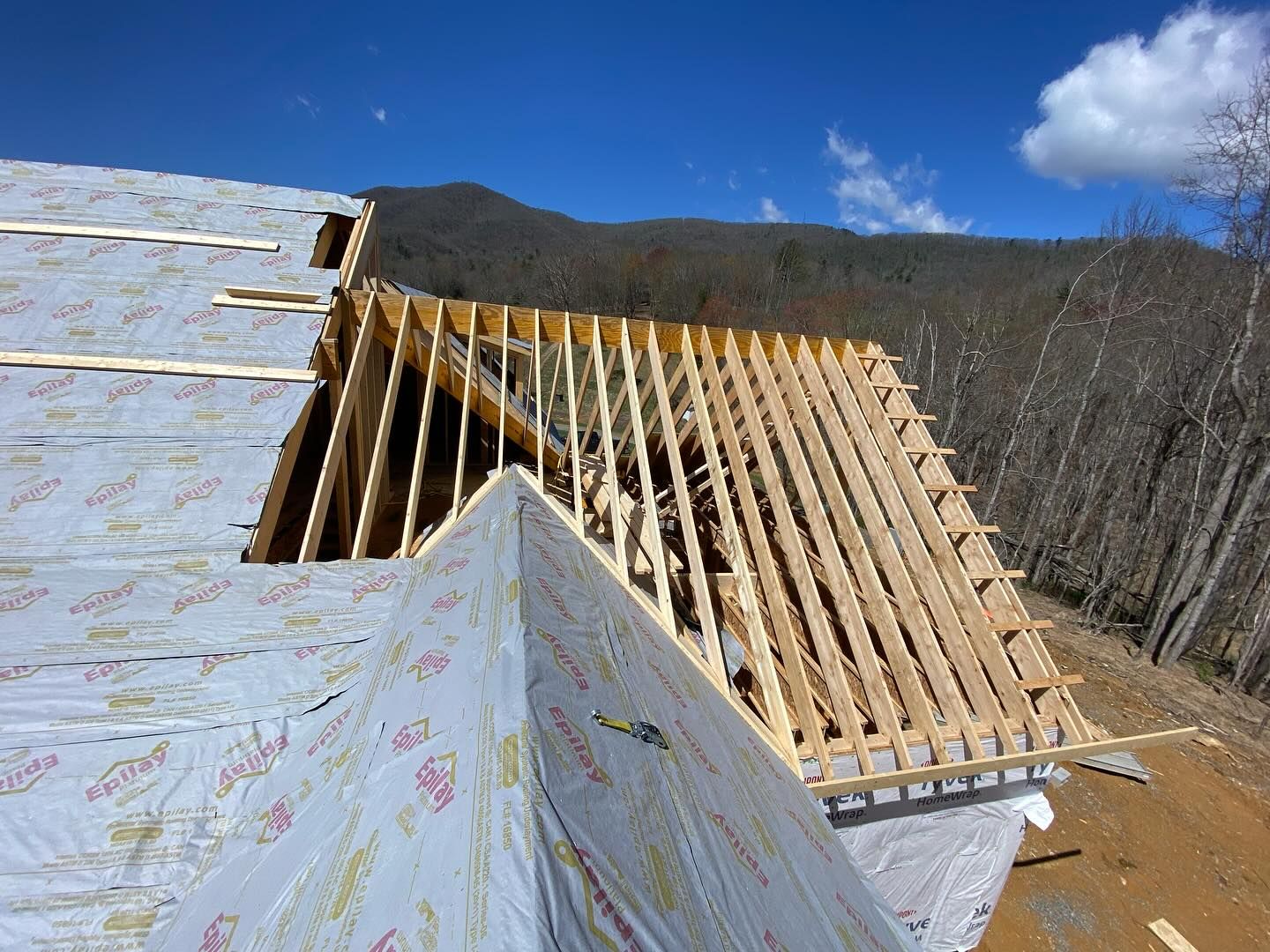 Roof under construction with wooden frame, vapor barrier, and mountain backdrop.