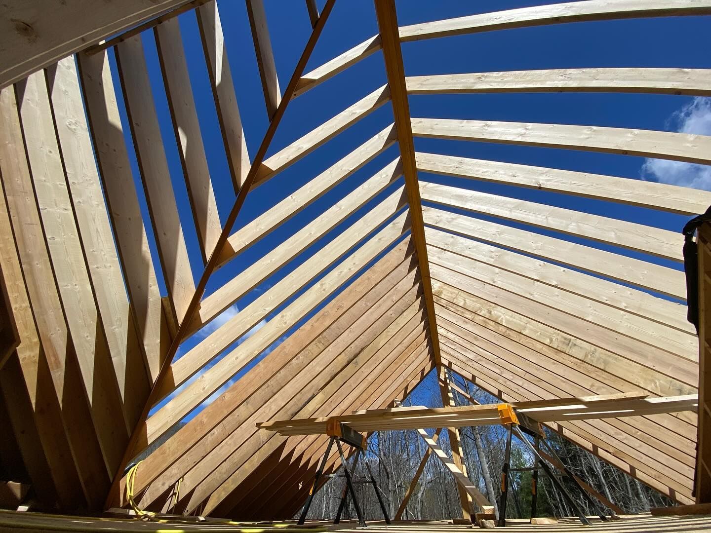 Wooden roof frame under construction against a bright blue sky.