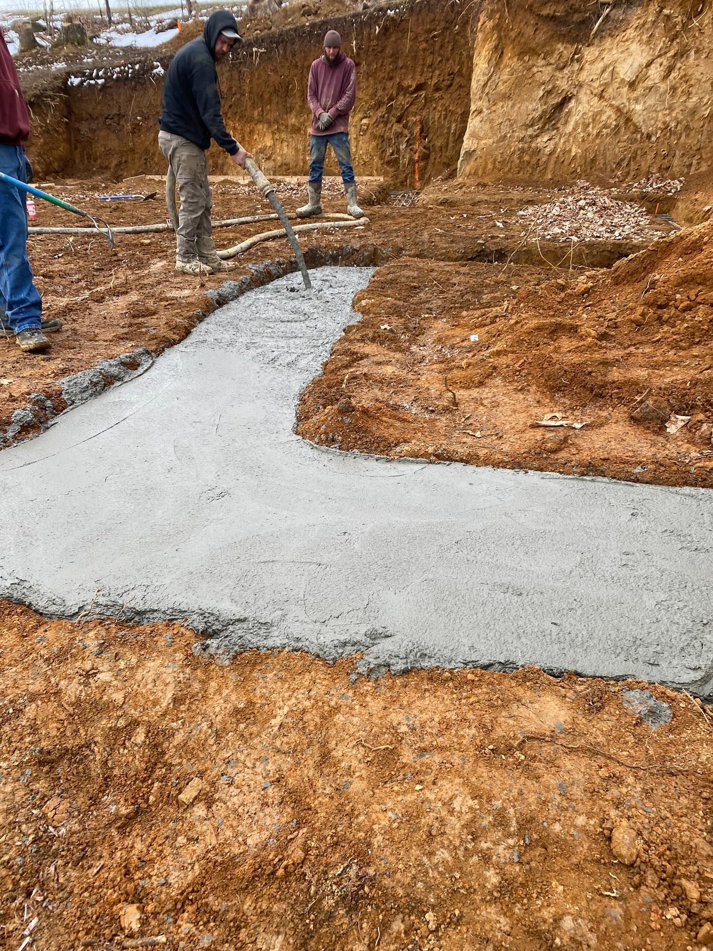 Workers smoothing concrete foundation in a dirt trench, outdoors.