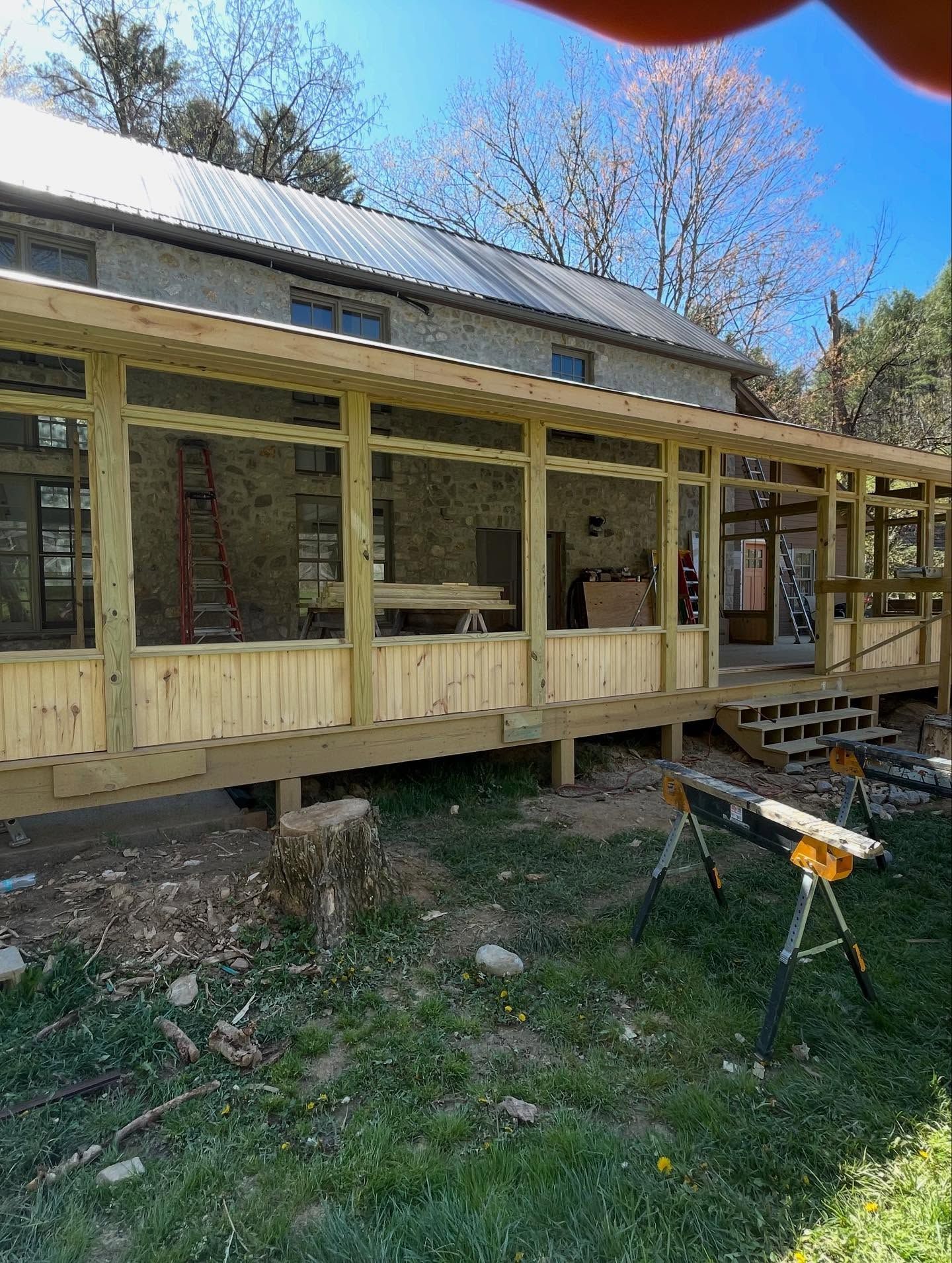 A wooden porch addition on a stone house with a metal roof.  Green grass and sunny day.