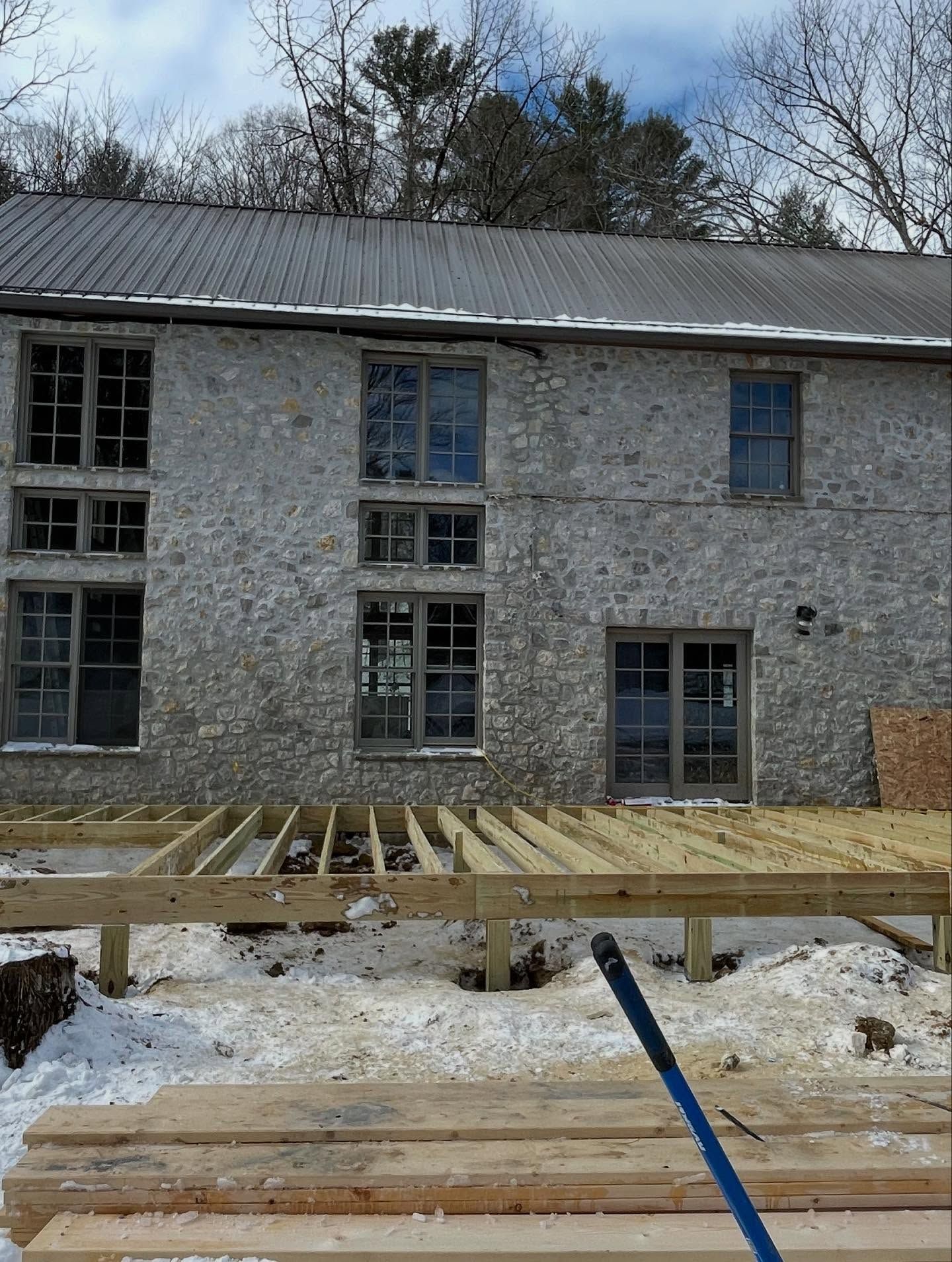 Exterior view of a stone building with new wooden deck under construction in a snowy setting.