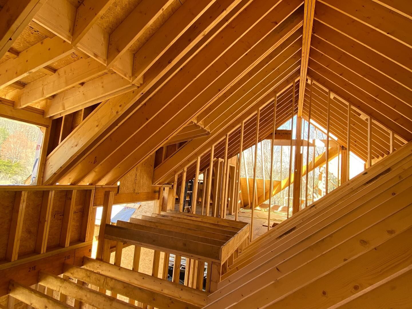 Wooden roof framing under construction, interior view, sunlight streams through openings.