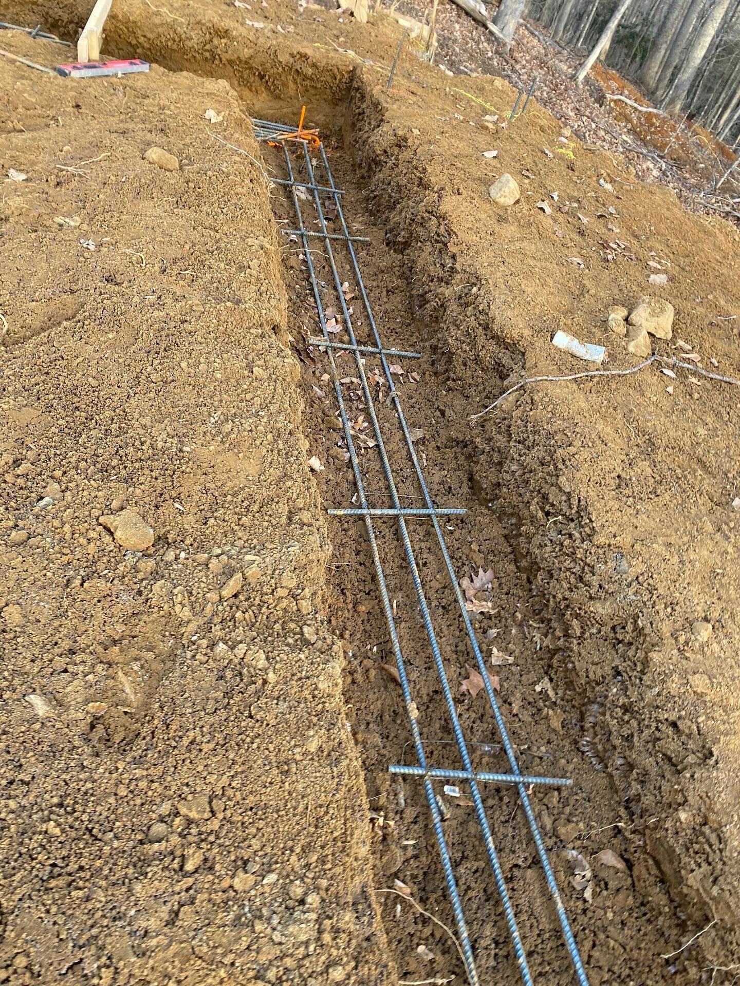 Trench dug in dirt, with steel rebar framework in place, ready for concrete foundation pour.