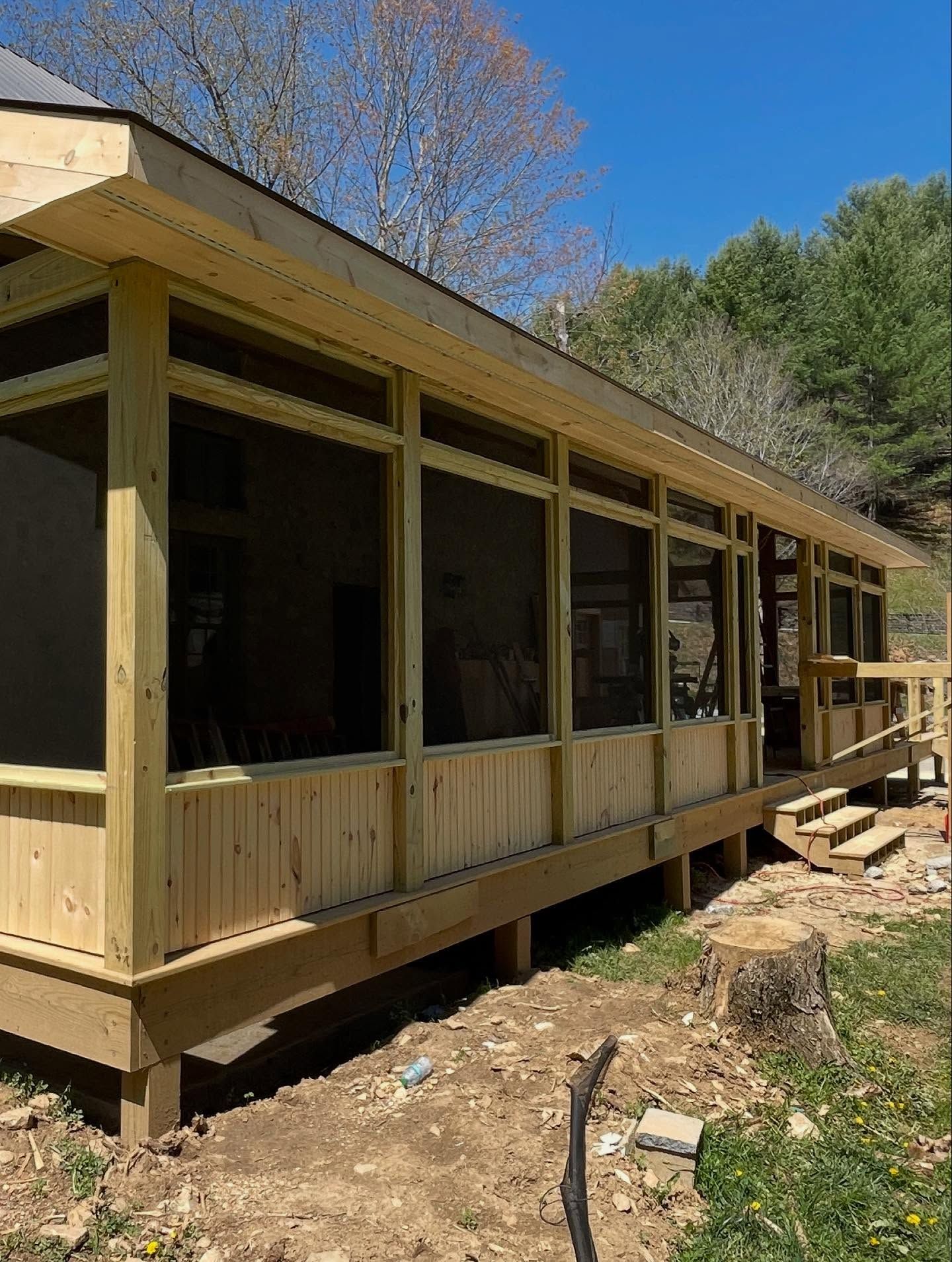 A newly constructed wooden screened porch with a deck, in a sunny outdoor setting.