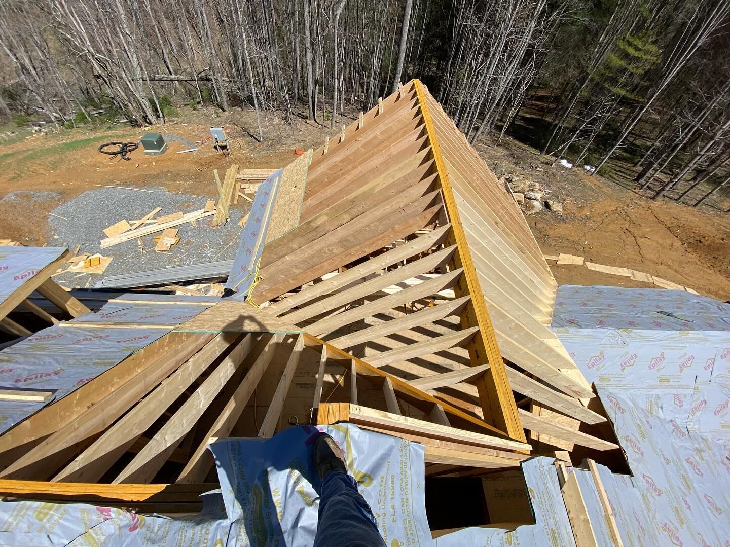 View from a roof construction site, showing wooden roof trusses being built; forest in the background.