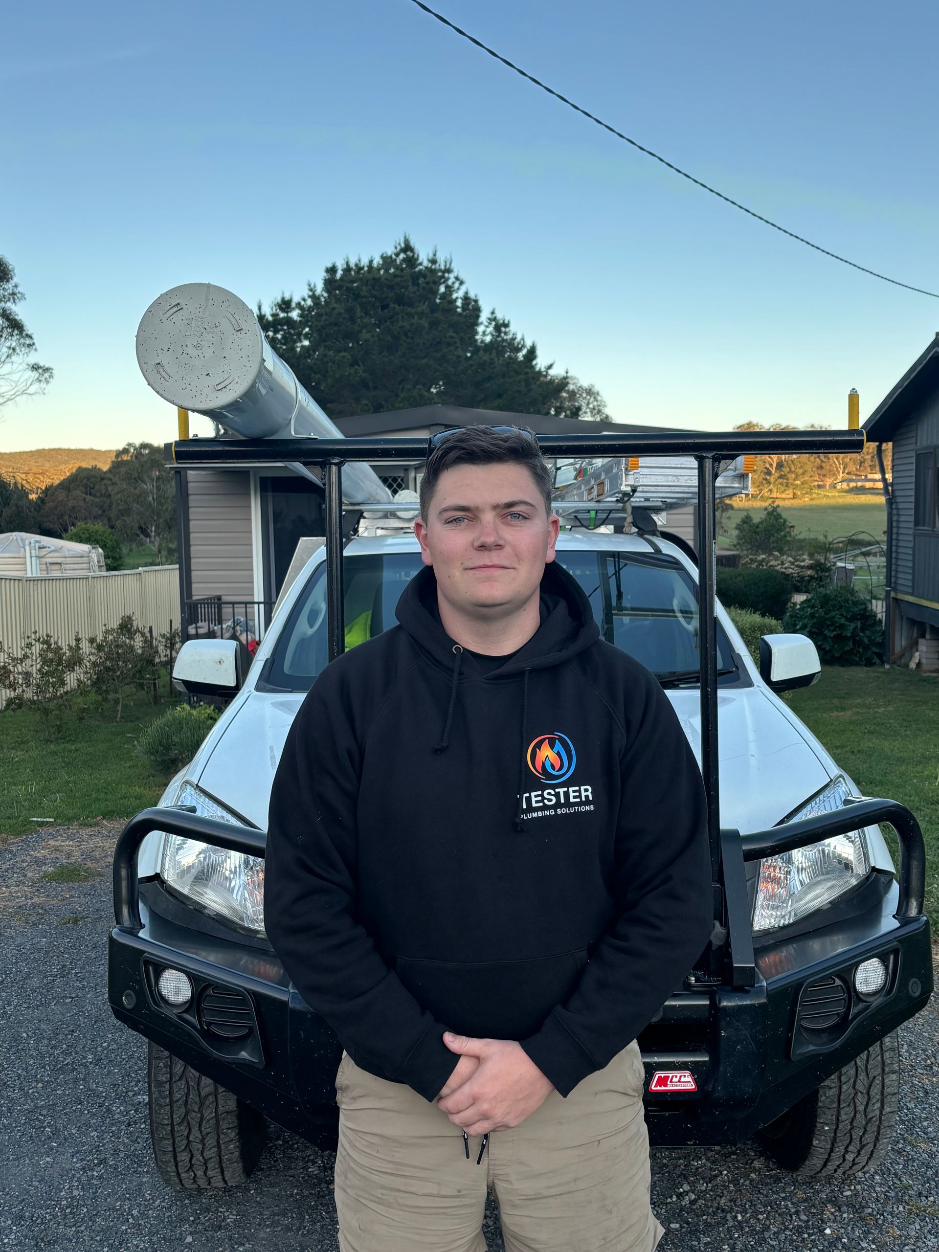 Man in black hoodie stands in front of a white truck with equipment on the roof.