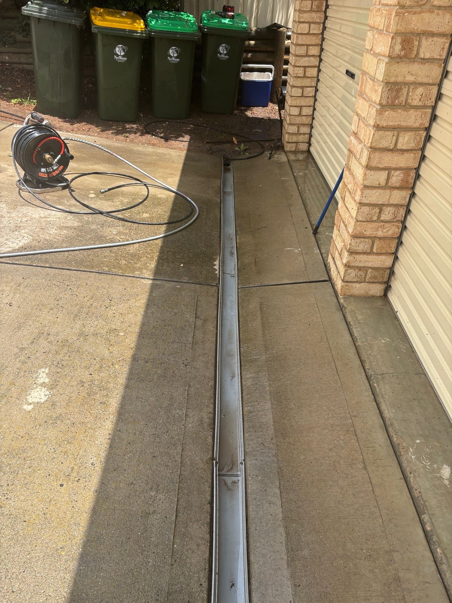 Pressure washer cleaning a concrete driveway; garage, trash cans in background.