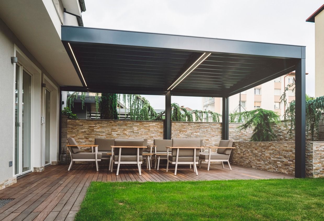 Outdoor patio with dark pergola, dining table, chairs, and stone wall; green lawn.