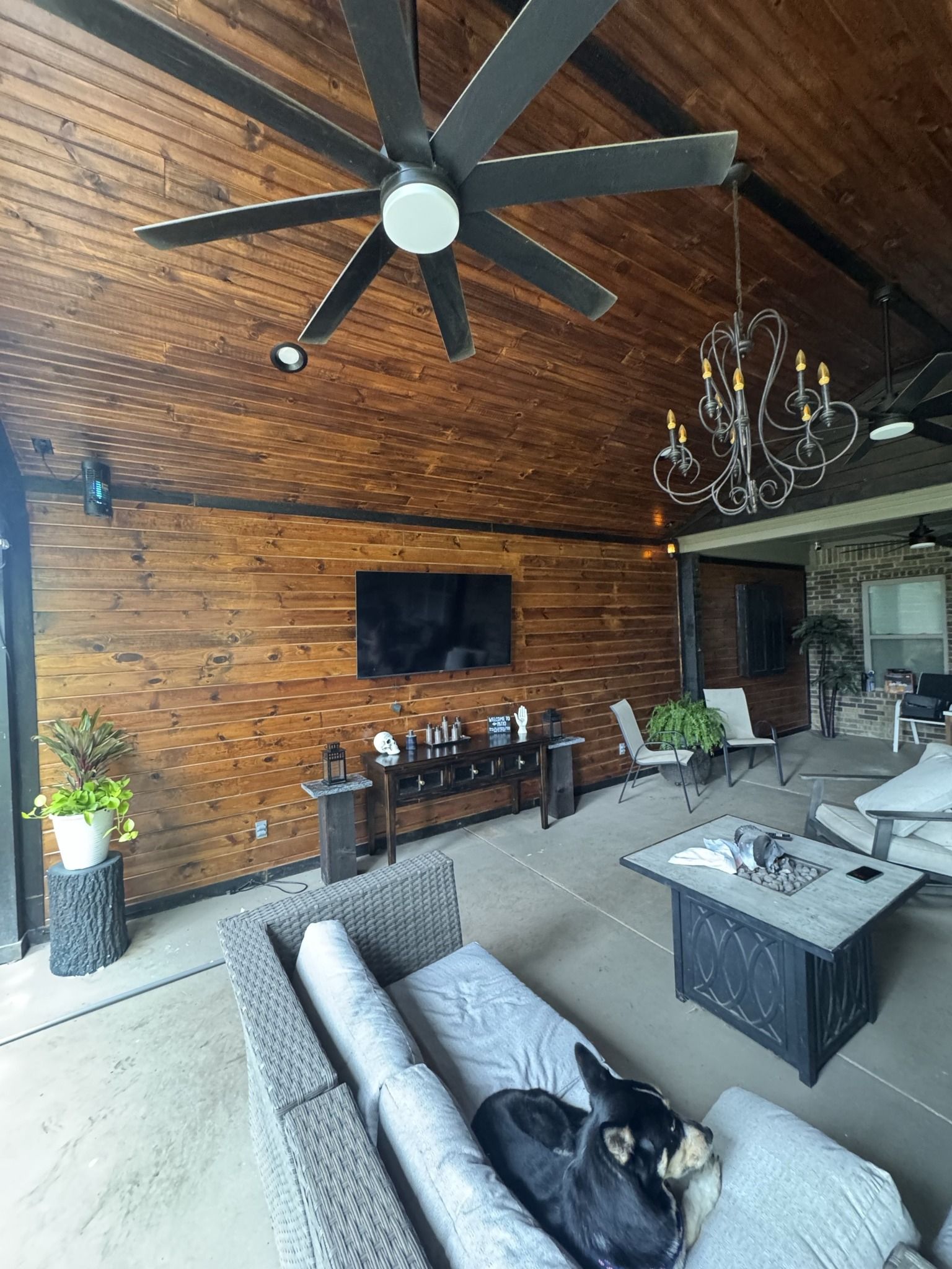 Outdoor patio with wood paneling, TV, dog, furniture, ceiling fan, and chandelier.
