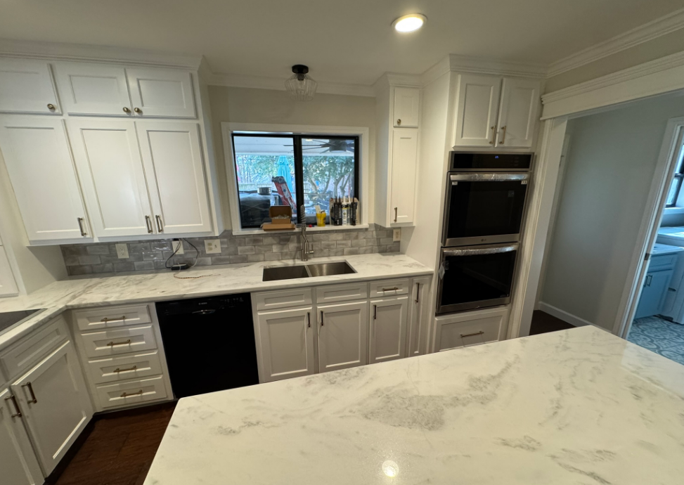 White kitchen with marble countertops, black appliances, and double ovens.