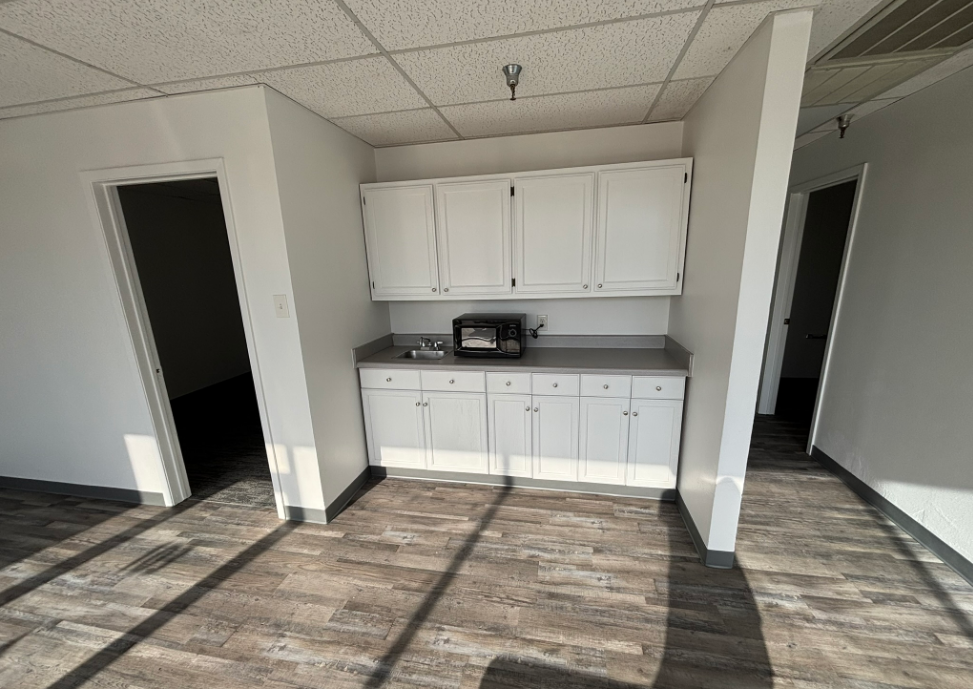 Empty room with white cabinets, countertop, and microwave. Two doorways on either side.