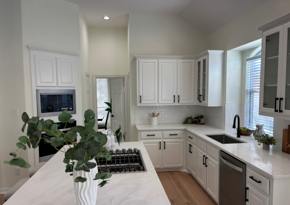 White kitchen with marble countertops, stainless steel appliances, and black hardware.