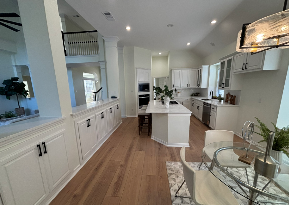 White kitchen with hardwood floors, cabinets, island, and dining area.