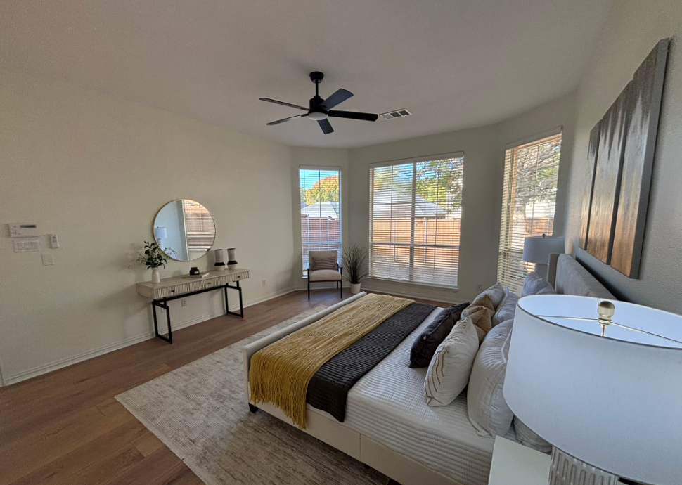 Bedroom with bed, rug, vanity, chair, windows, and a ceiling fan.