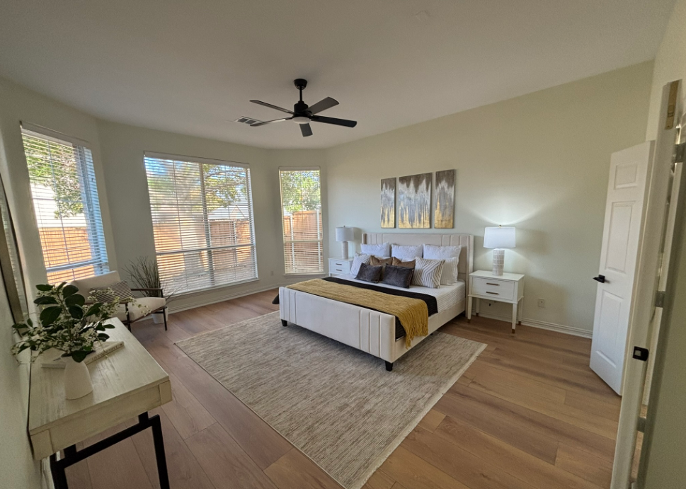 Bedroom with a white bed, beige rug, and large windows.  Wooden floors and neutral walls.
