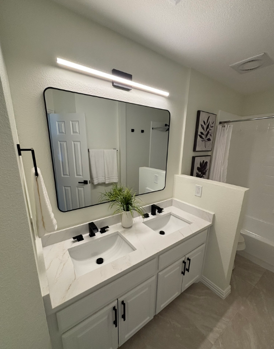 Modern white bathroom with double sink vanity, black fixtures, and framed mirror.