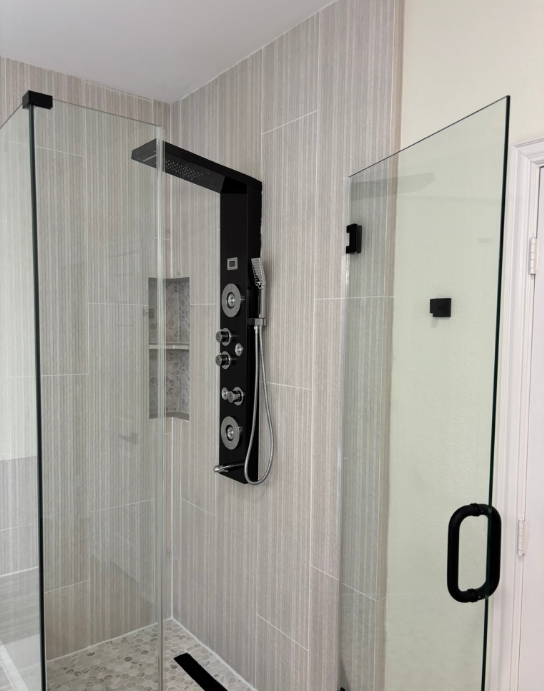 Modern shower with a black shower panel, glass door, and light-colored tiled walls.