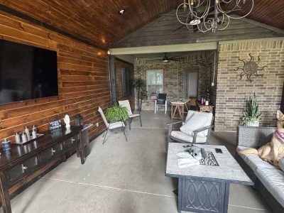 Covered patio with TV, furniture, brick wall, and dog.