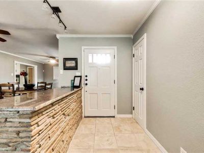 Entryway with white door, stone-faced island, gray walls, and light tile flooring.