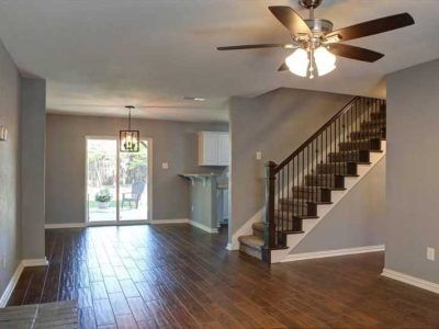 Living room with hardwood floors, stairs, and a sliding glass door to a backyard. Grey walls and a ceiling fan.