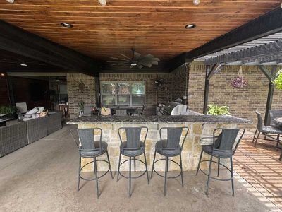 Outdoor bar with stone facade, granite countertop, and metal bar stools under a wooden ceiling.