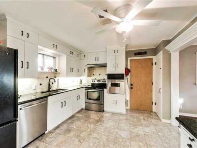 White kitchen with stainless steel appliances, black countertops, and light-colored tiled floor.