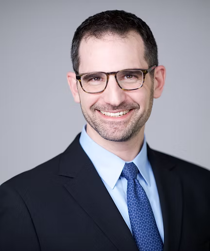 Smiling woman with two-toned dark and blonde hair wearing a grey blazer against a neutral backdrop.
