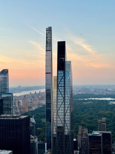 Two towering, slender skyscrapers overlook Central Park in New York City at sunset.