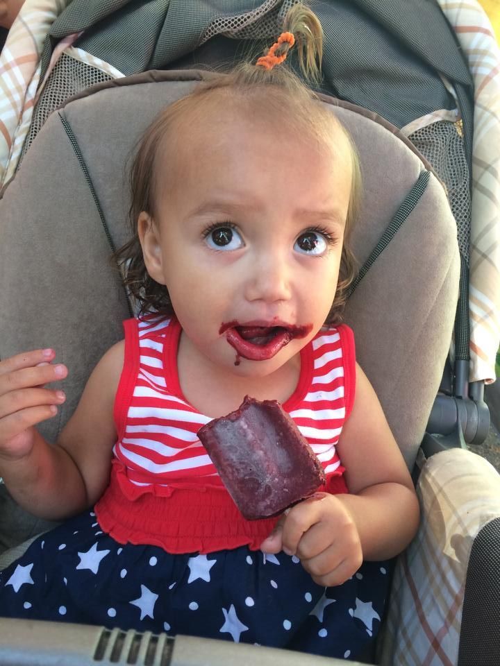A little girl is sitting in a high chair eating a popsicle