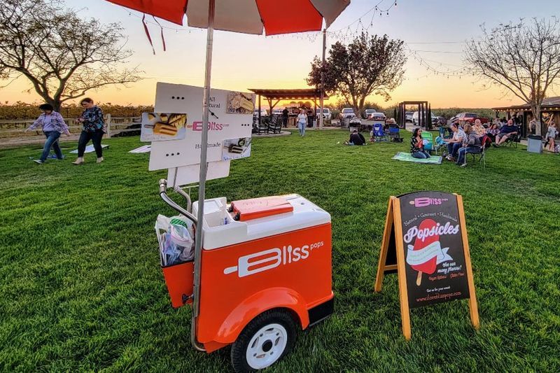 An ice cream cart is parked in the grass next to a sign.