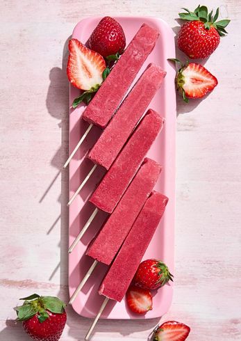 A pink plate topped with strawberry popsicles and strawberries.